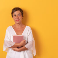 woman standing in front of yellow wall holding a book