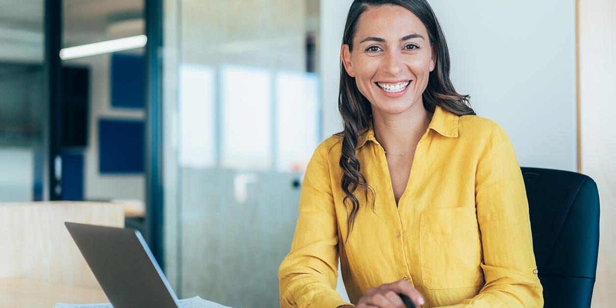 Women in office with laptop smiling at camera
