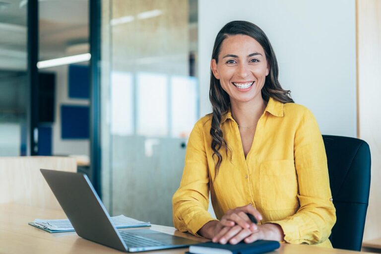 2025 Minimum Wage Change Women in office with laptop smiling at camera