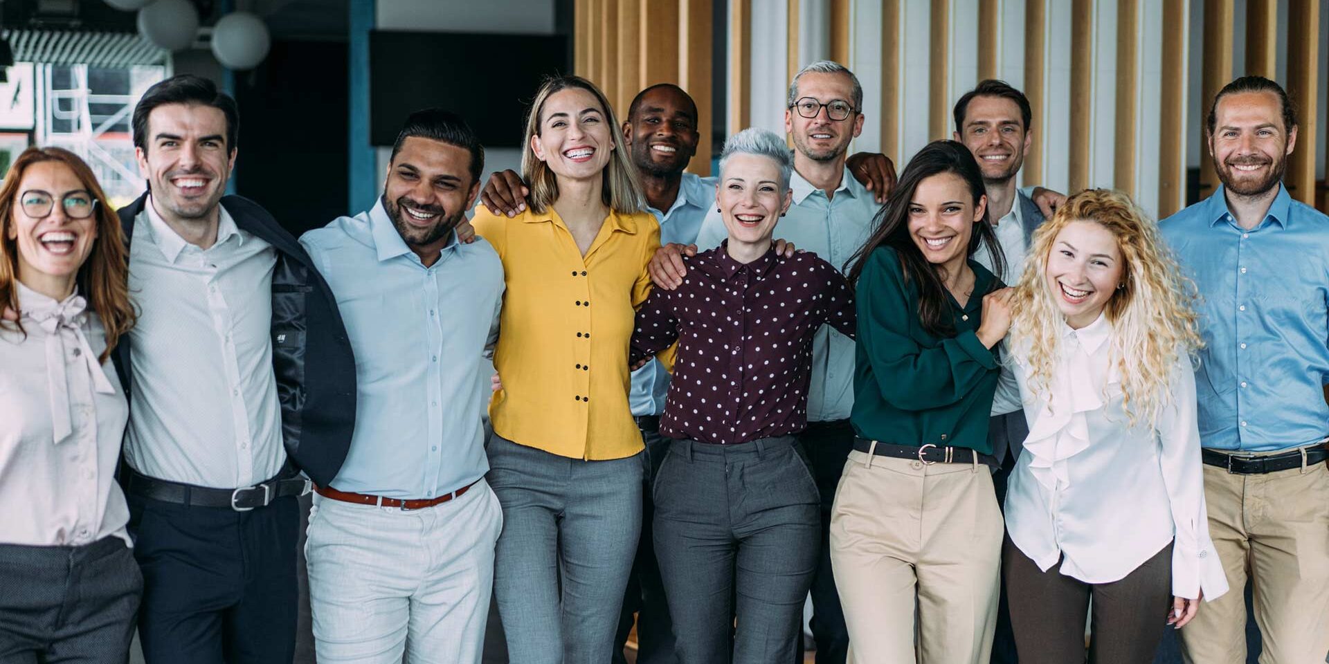 11 work colleagues standing arm in arm smiling at camera